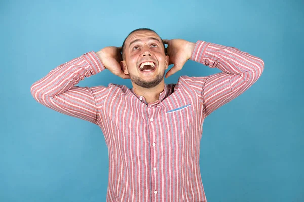 Rus iş adamı mavi arka planda rahatlıyor ve esniyor, kolları ve elleri başının arkasında mutlu bir şekilde gülümsüyor.