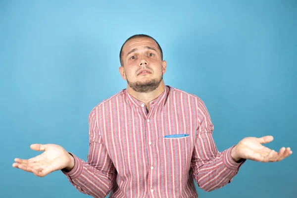 Mavi arka planda kırmızı tişört giyen Rus iş adamı elleri ve kolları havada, kafası karışmış bir ifade takınıyor.