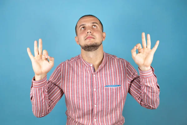 Rus iş adamı mavi arka planda rahatlayıp gözleri kapalı parmaklarıyla meditasyon hareketi yaparken gülümsüyor. Yoga konsepti.