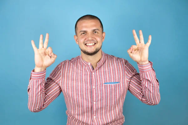 Rus iş adamı mavi arka planda olumlu bir şekilde iki elinle ve parmaklarınla imza atıyorsun. Başarılı ifade