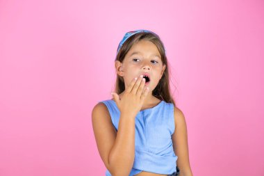 Soyutlanmış pembe arka planda genç ve güzel bir kız çocuğu. Elle ağzını kapatmaktan sıkılmış. Huzursuz ve uykulu..