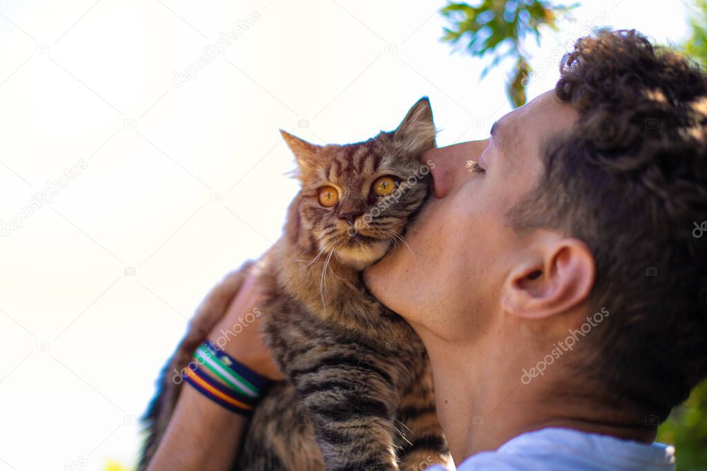 Young handsome man in the garden hugging and kissing a cat