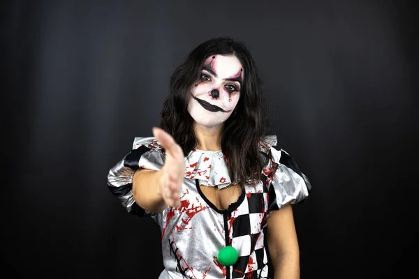 woman in a halloween clown costume over isolated black background smiling friendly offering handshake as greeting and welcoming