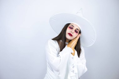 İzole edilmiş beyaz arka plan üzerinde cadı kostümü giyen kadın yorgun uyuyor ve elleri ile birlikte poz verirken gözleri kapalı gülümsüyor..