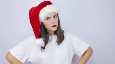 Noel Baba şapkası takan genç ve güzel bir kadın izole edilmiş beyaz arka planda çok kızgın ve kameraya hayır diyor.