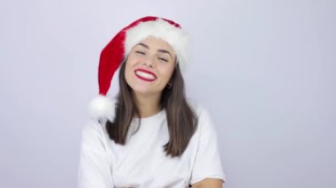 Noel Baba şapkası takan genç ve güzel bir kadın izole edilmiş beyaz arka planda süper mutlu, kameraya gülümsüyor.