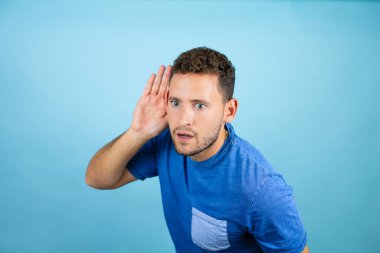 Mavi arka planda mavi tişört giyen yakışıklı bir genç adam. Kulağından kulağa gülümsüyor. Dedikoduları ve dedikoduları dinliyor.