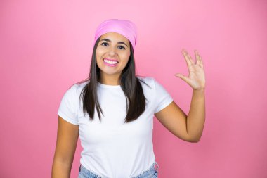 Pembe başörtüsü takan genç ve güzel bir kadın izole edilmiş pembe arka planda Star Trek ucube sembolü yapıyor.