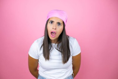 Pembe başörtüsü takan genç ve güzel bir kadın pembe arka planda korku ve şaşkınlık dolu bir ifade, korku ve heyecan dolu bir yüz..