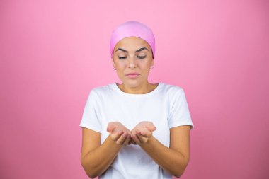 Pembe başörtüsü takan genç ve güzel bir kadın pembe arka planda avuçlarıyla gülümsüyor ya da el hareketi yapıyor. Tutun ve koruyun