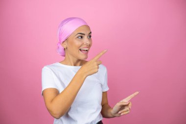 Pembe başörtüsü takan genç ve güzel bir kadın pembe arka planda şaşırmış ve parmaklarını işaret ediyor.