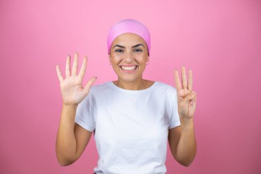 Pembe başörtüsü takan genç ve güzel bir kadın pembe arka planda kendini güvende ve mutlu hissederken sekiz numaralı parmaklarıyla işaret ediyor.