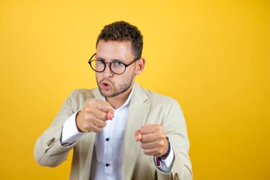 Genç yakışıklı iş adamı sarı arka planda takım elbise giyiyor. Yumruk yumruğa dövüşme, agresif ve öfkeli saldırı, tehdit ve şiddet.