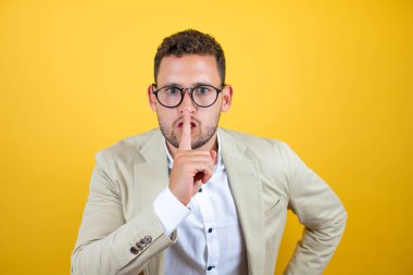 Soyutlanmış sarı arka planda takım elbiseli genç ve yakışıklı iş adamı sessiz olmak istiyor. Sessizlik ve gizli konsept.