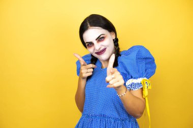 Sarı arka planda korkunç bir cadılar bayramı kostümü giyen kadın seni ve kamerayı işaret ediyor.