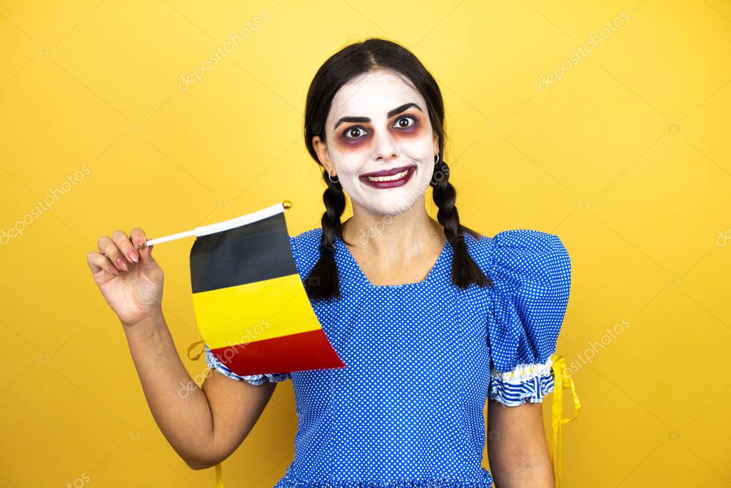 woman wearing a scary doll halloween costume over yellow background holding the Belgium flag