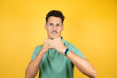 Sarı arka planda yeşil tişört giyen yakışıklı genç adam dövüşmek için yumruk, agresif ve öfkeli saldırı, tehdit ve şiddet.