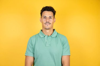 Sarı arka planda yeşil tişört giyen yakışıklı genç adam gülümsüyor ve kameraya bakıyor.