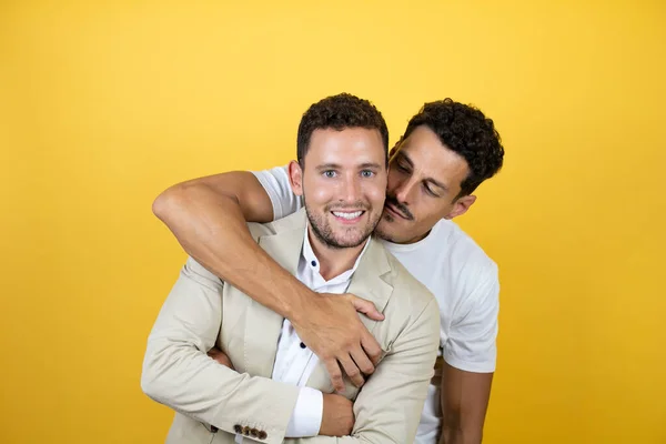 若いですゲイカップルの二人の男身に着けていますカジュアル服上の隔離された黄色の背景立ちますとともに笑顔上の顔巨大 — ストック写真