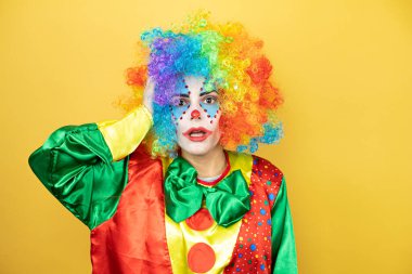 Sarı arka planda dikilen palyaço bir elini kafasına koyup sanki bir şey unutmuş gibi gülümsüyordu.