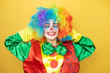 Sarı arkaplanda dikilen soytarı rahatlıyor ve esniyor, kolları ve elleri başının arkasında mutlu bir şekilde gülümsüyor.