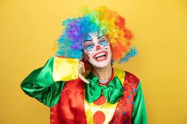 Sarı zemin üzerinde duran palyaço gülümsüyor telefonla el ve parmak hareketleri yapıyor telefonda konuşuyor gibi.