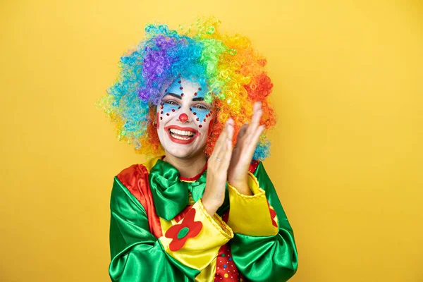 Sarı arkaplanda duran palyaço alkışlıyor ve alkışlıyor mutlu ve neşeli, gülümseyen gururlu eller birlikte.