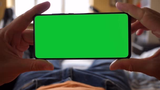 Sosteniendo un Smartphone de pantalla verde mientras está acostado en la cama — Vídeos de Stock