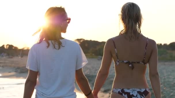 Una pareja de lesbianas caminando en la playa al atardecer — Vídeos de Stock