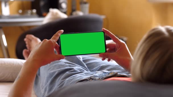 Mujer sosteniendo un teléfono inteligente horizontal de pantalla verde, acostado en la cama — Vídeos de Stock