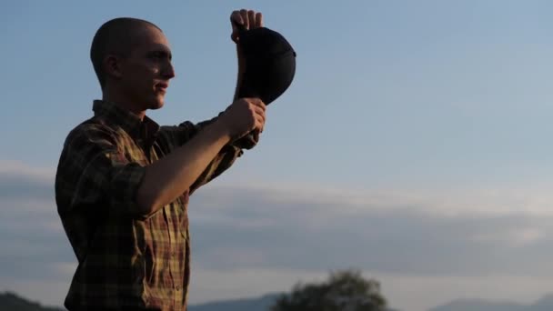 年轻的农民在日落时戴上棒球帽，动作缓慢 — 图库视频影像