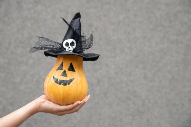 Şapkada balkabağı tutan kadın eli mi yoksa gri arka planda balkabağı feneri mi? Şükran Günü Cadılar Bayramı, tatil dekorasyonu konsepti. Boş kopyalama alanı.