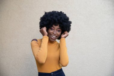 Mutluluğun yatay görüntüsü kıvırcık saçlı Afro-Amerikan kadın, zafer jestinde yumrukları sıkmak, müthiş bir olay, gündelik giysiler giymek, açık arka planda poz vermek.