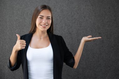 Gülümseyen genç iş kadını, gri arkaplanda reklam sloganı ya da kısa mesaj için bazı ürünler ya da boş telif alanları gösteriyor. İş başarısı konseptinde Kafkas modeli.