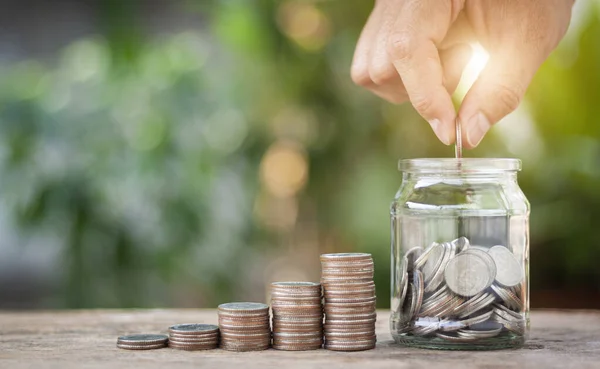 Hand putting coins in the jar on wooden table. The concept of saving money, finance, business and investment is growing in the future.