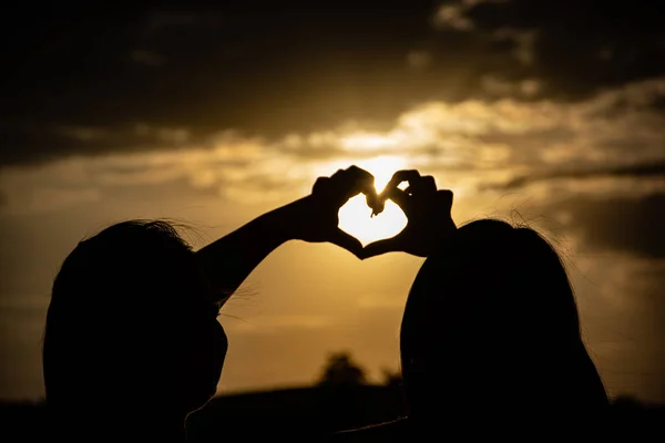 Kız Kardeşler Ellerini Günbatımının Arka Planında Kalp Şeklinde Tutarlar — Stok fotoğraf