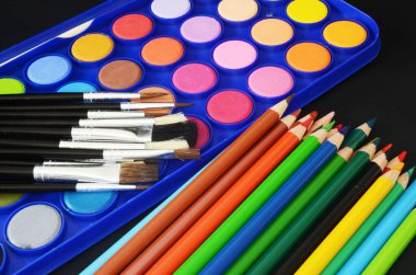 renk kalemleri, boya fırçaları ve suluboya palet, okula geri dönüş malzemesi, okula dönüş, koyu arkaplanda renkli kalemler.