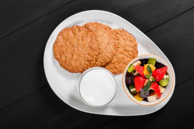 Yoğurt meyve salatası ve yulaf kurabiye plaka üzerinde koyu ahşap arka plan ile. Taze sağlıklı kahvaltı. Üstten görünüm