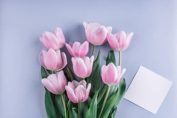 Pink tulips flowers and sheet of paper over light blue background. Greeting card or wedding invitation. Flat lay, top view, copy space — Stock Image Pink Tulips Flowers Sheet Paper Light Blue Background Greeting Card Stock Photo