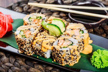 Suşi kara taş üzerine bambu hasır, seçici odak üzerinde set karides tempura, salatalık, soğan, avokado ve susam ile alır. Japon mutfağı