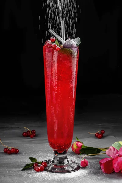 Cold red cocktail with red currant, orange and ice in tall glass on dark background. Summer drinks and alcoholic cocktails