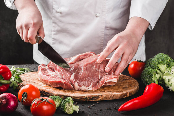 Chef Butcher cutting pork meat with knife on kitchen, cooking food