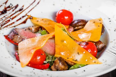 Sığır eti biftek chargrilled Orta nadir kiraz domates, mantar ve peynir koyu ahşap zemin üzerine sıcak salata. Sıcak et yemekleri. Maddeler tablosundaki. Üstten görünüm