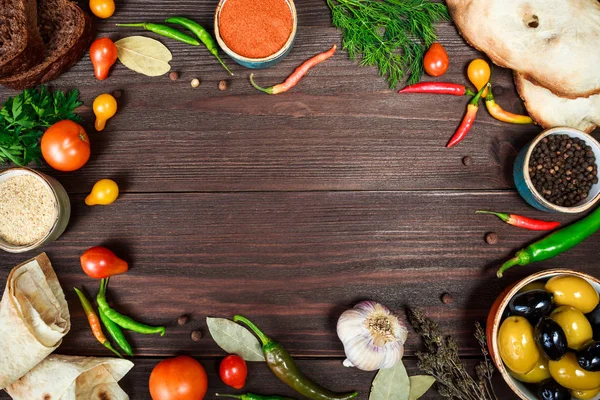 Culinary wooden background with fresh farm vegetables, olives, bread, pita, grain tortillas and spices. Food background top view.