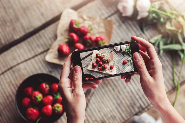 Girl\'s hands taking photo of breakfast with strawberries by smartphone. Healthy breakfast, Clean eating, vegan food concept.