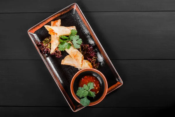 Stuffed crepes topped with vegetables and sauce in plate on dark wooden background. Healthy breakfast. Top view.