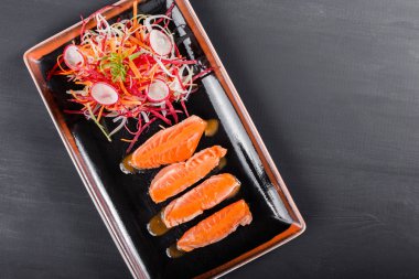 Koyu arka plan üzerinde siyah plaka üzerinde sos ve sebze salatası ile somon fileto. Lezzetli yemek deniz ürünleri. Üstten görünüm.