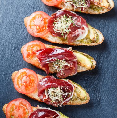 Meze bruschetta salam, domates, kabak ciabatta ekmeği taş arduvaz arka plan üzerinde tarih ile kapatın. Lezzetli aperatifler, sandviçler, crostini, parti ya da piknik zamanında antipasti. Üstten Görünüm