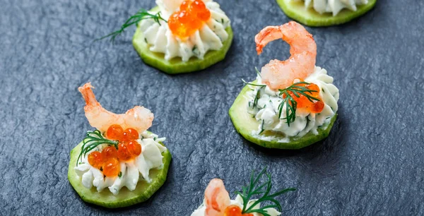Appetizer canape with red caviar, shrimp and cream cheese on stone slate background close up. Delicious snacks, sandwiches, crostini, bruschetta, antipasti on party or picnic time. Top view