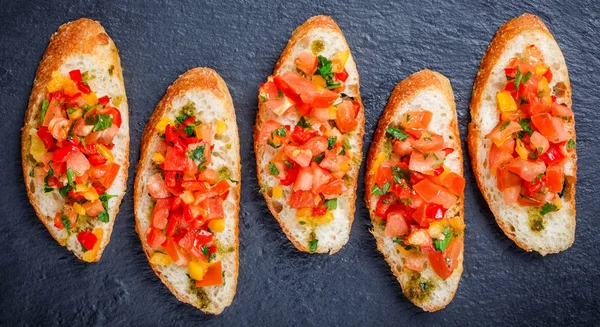 Appetizer bruschetta with chopped vegetables on ciabatta bread on stone slate background close up. Delicious snacks, sandwiches, crostini, canape, antipasti on party or picnic time. Top view